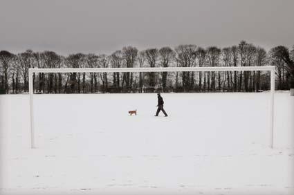 A man walks his dog over Old Malton St Mary FC's pitch, after their match against Copmanthorpe was called off on another weekend in which sporting action was decimated by the wintry weather.