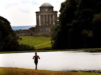 A competitior in the Castle Howard Triathlon is silhouetted against the lake with the mausoleum in the background.
