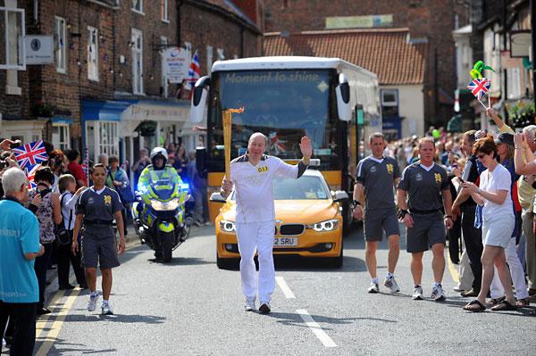 Eugene Perry carries the Olympic Flame on the Torch Relay leg through Thirsk