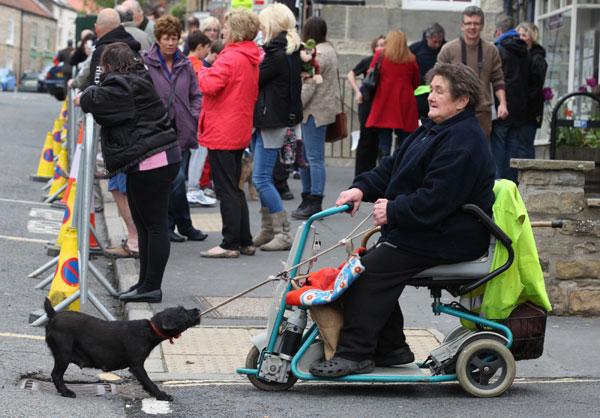 A woman in a disability scooter is pulled along by her dog through the crowds gathering to watch the Kirkbymoorside 10k race.