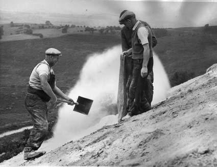 On a windy day workmen attempt to spread lime on the white horse at Kilburn.
