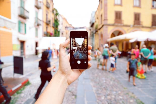 Gazette & Herald: A tourist taking a picture of a busy street on their phone. Credit: Canva