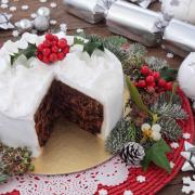 A traditional Christmas cake with holly, bauble decorations and winter greenery over oak background