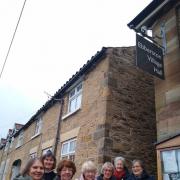 Members of  Ebberston and Allerston WI, pictured beneath the newly erected sign for Ebberston village hall showing the detail in the handcrafted metalwork of the letters ‘WI’ and the number ‘104’ to signify the number of years the